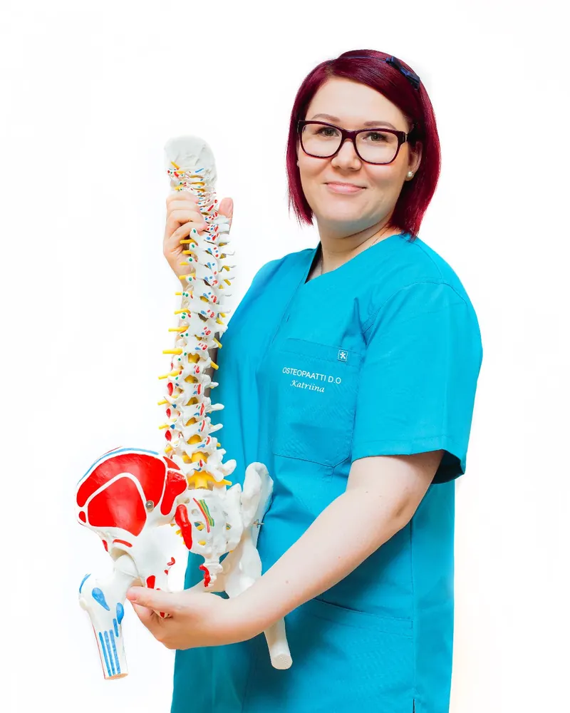 Katriina Slotte turkoosissa työasussa pitelee selkärangan ja lantion anatomiamallia